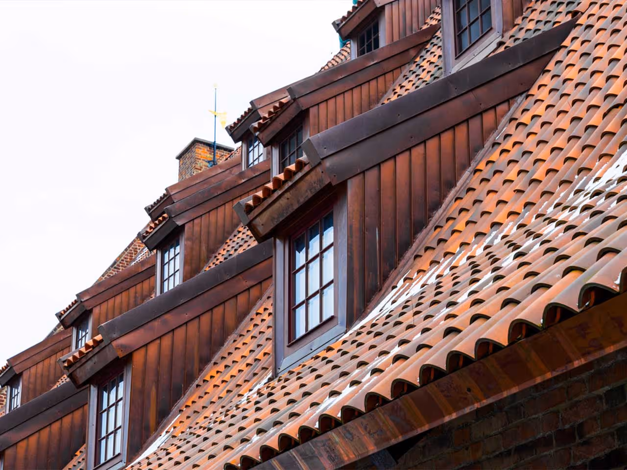 Close-up of a roof with brown wooden dormer windows and reddish clay roof tiles.