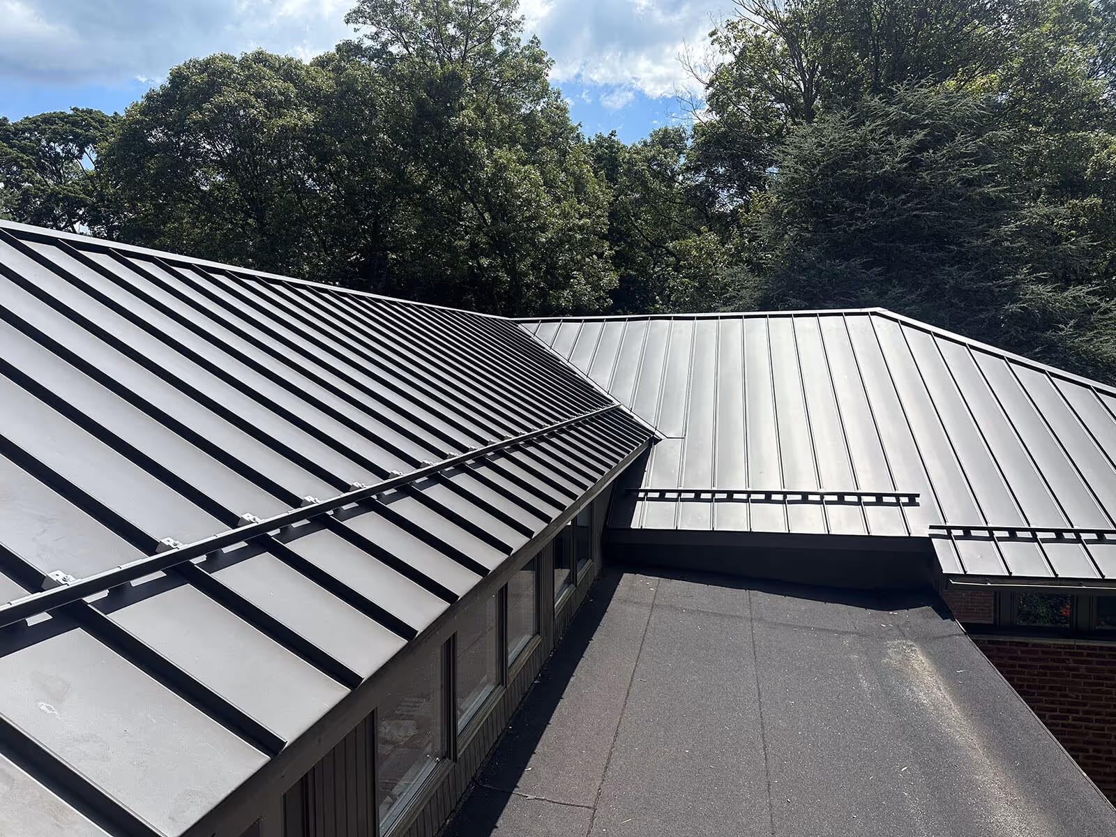 Black aluminum metal roofing panels on a residential building with trees in the background.