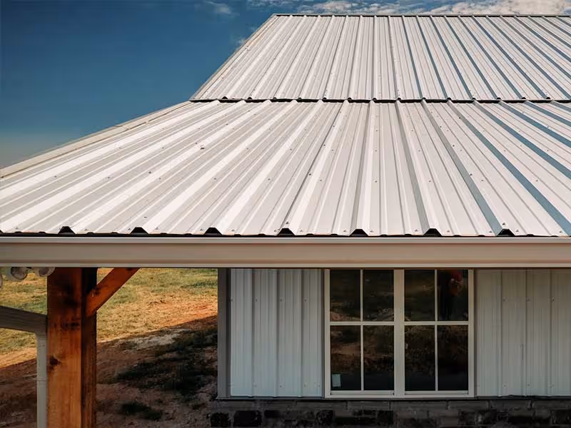 White corrugated metal roofing on a building with wood support beams and a window beneath.