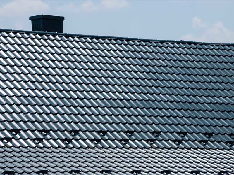 Close-up of shiny metal roofing tiles on a house roof under a blue sky.