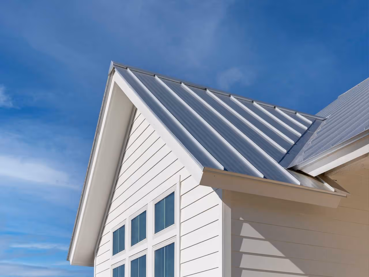 White house section with vertical aluminum metal roofing under a blue sky.