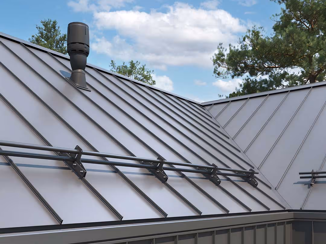 Gray standing seam metal roof with snow guards and a vent pipe under a partly cloudy sky.