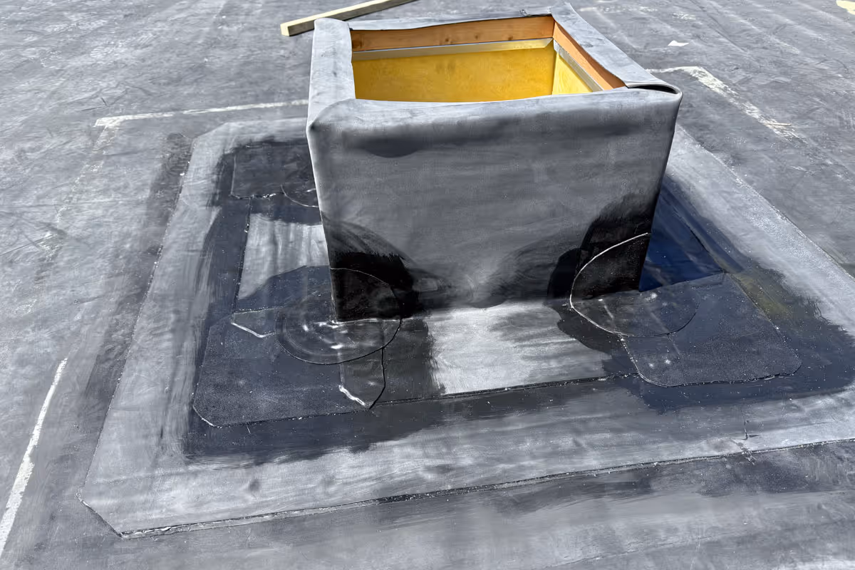 Flat roofing with sealed black waterproof membrane around a rooftop ventilation shaft.