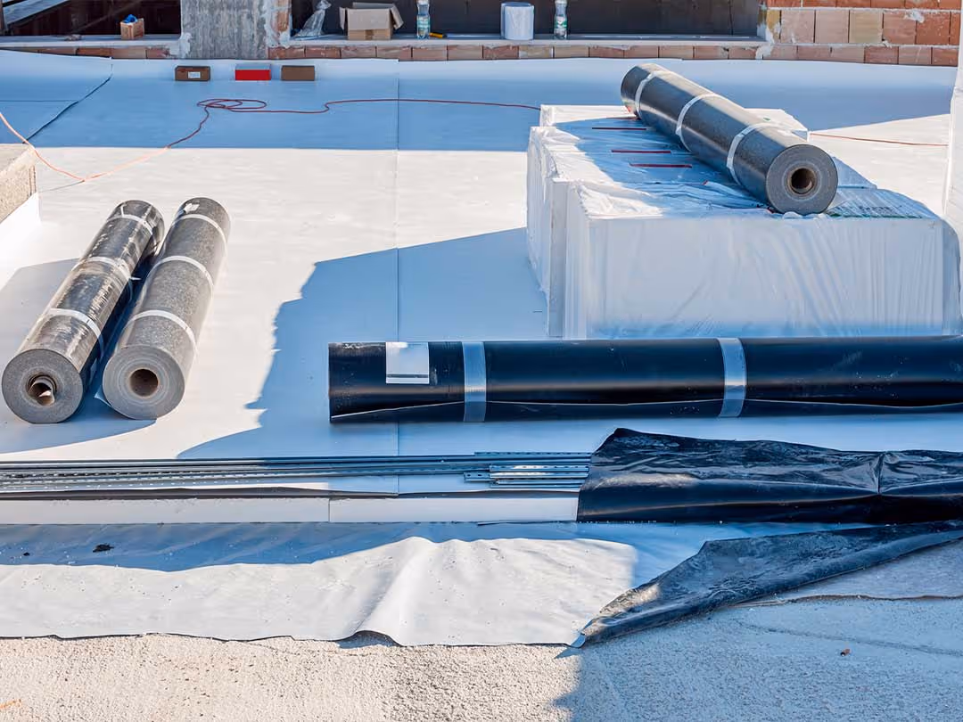 Flat rooftop under construction with rolls of black roofing material and insulated panels.