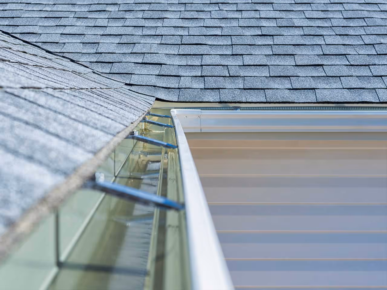 Close-up of a clean aluminum gutter along an asphalt shingle roof.