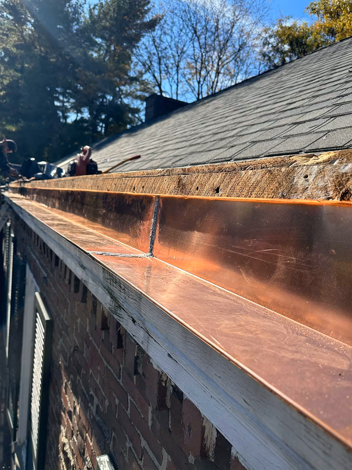 Close-up of newly installed shiny copper gutter on a house roof under clear sky.