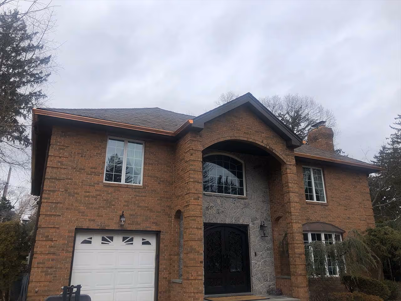 Brick two-story house with arched entrance, black double doors, white garage door, and copper gutters.