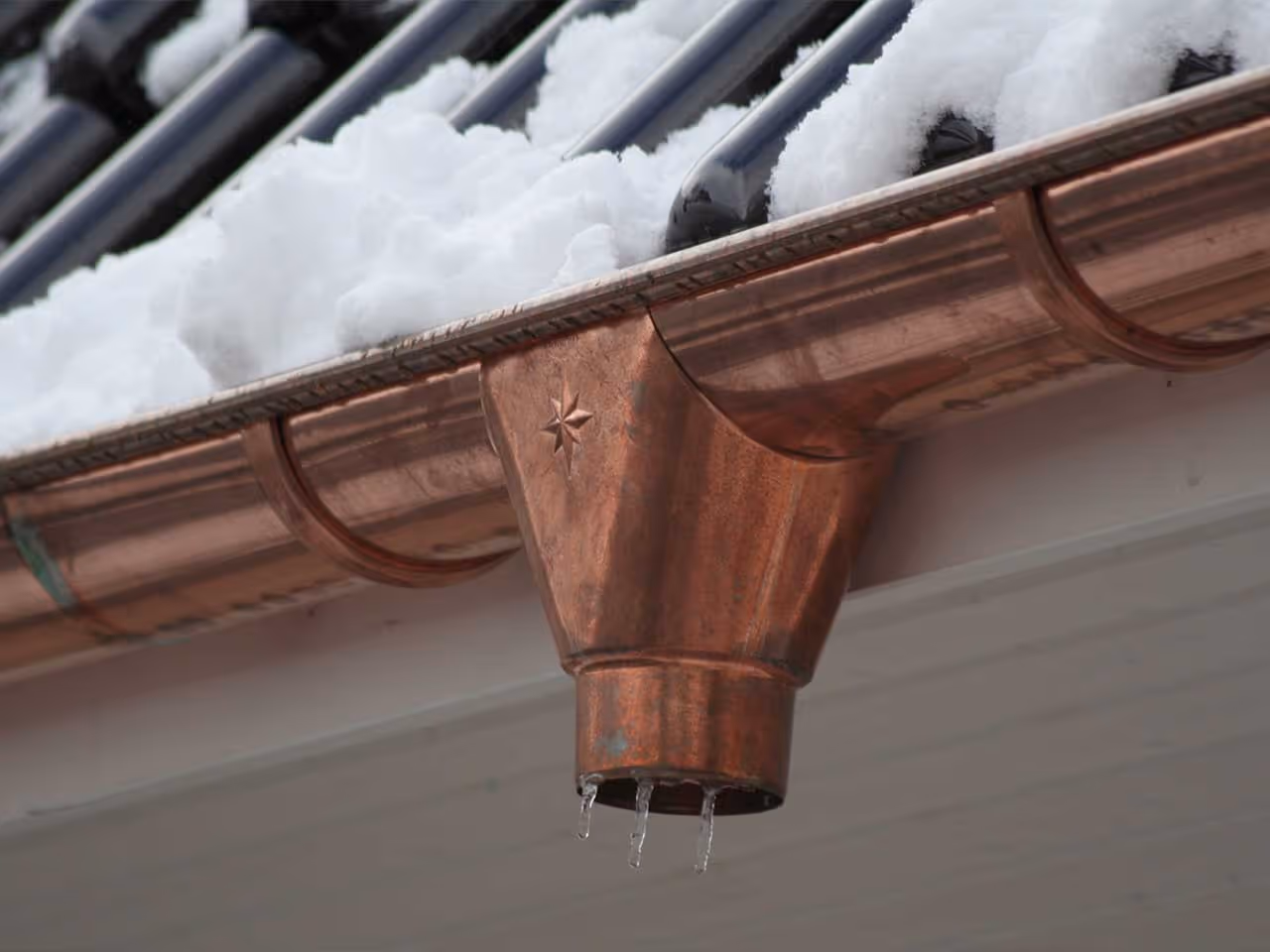 Copper gutter with a star pattern, snow on the roof, and icicles forming beneath.