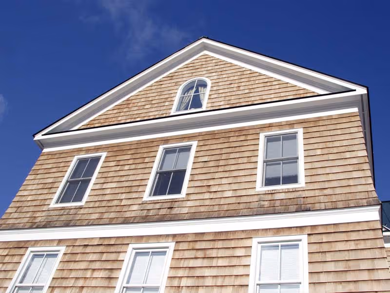 Close-up of a house exterior with natural cedar wood siding and white-framed windows under a blue sky.