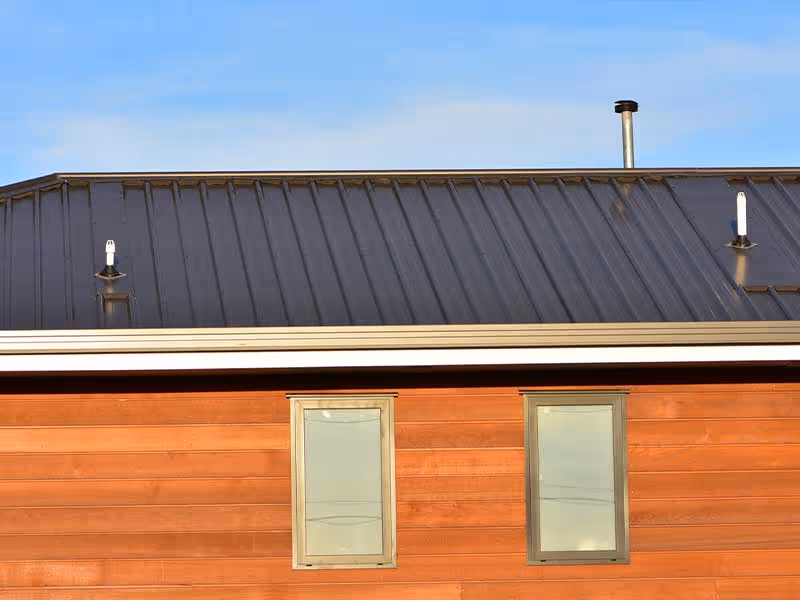 Close-up of house exterior with dark metal roof and two rectangular windows on reddish-brown wooden siding.
