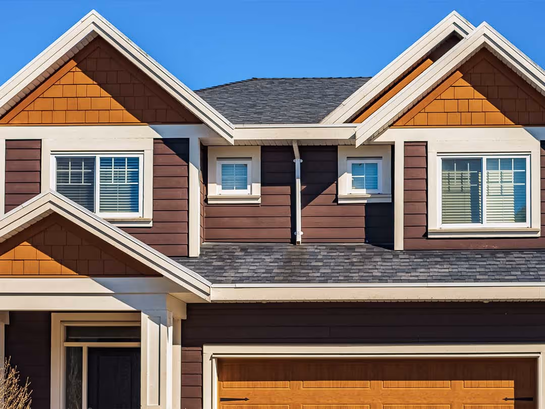 Two-story house exterior with brown cedar siding and orange gable accents under clear blue sky.