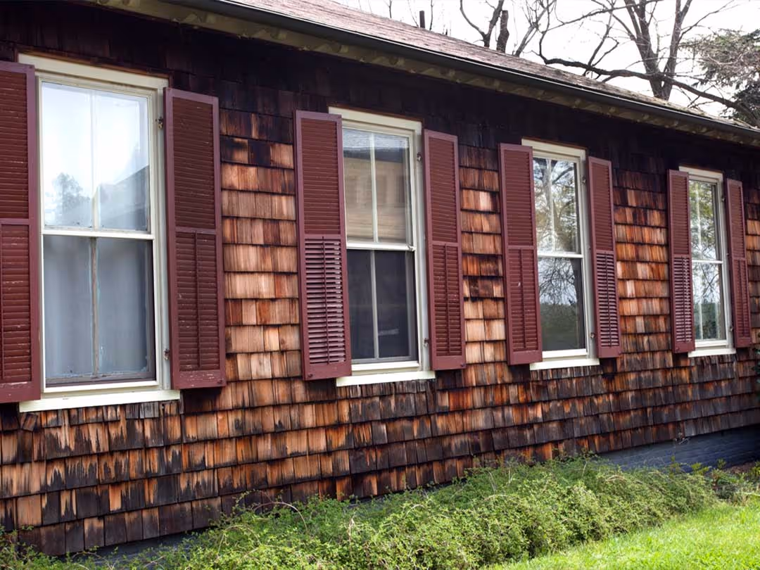 House exterior with cedar wood siding and four windows with maroon shutters.