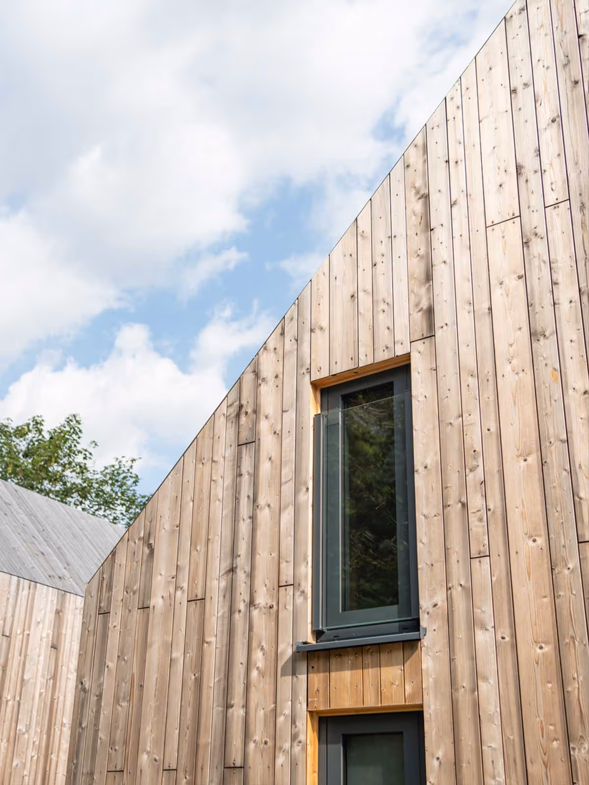 Modern building exterior featuring vertical cedar siding with tall narrow windows under a partly cloudy sky.