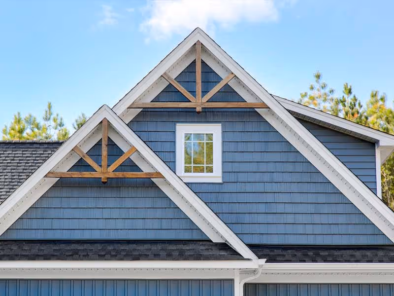 Blue house roof with white trim and wooden gable brackets against a clear sky.