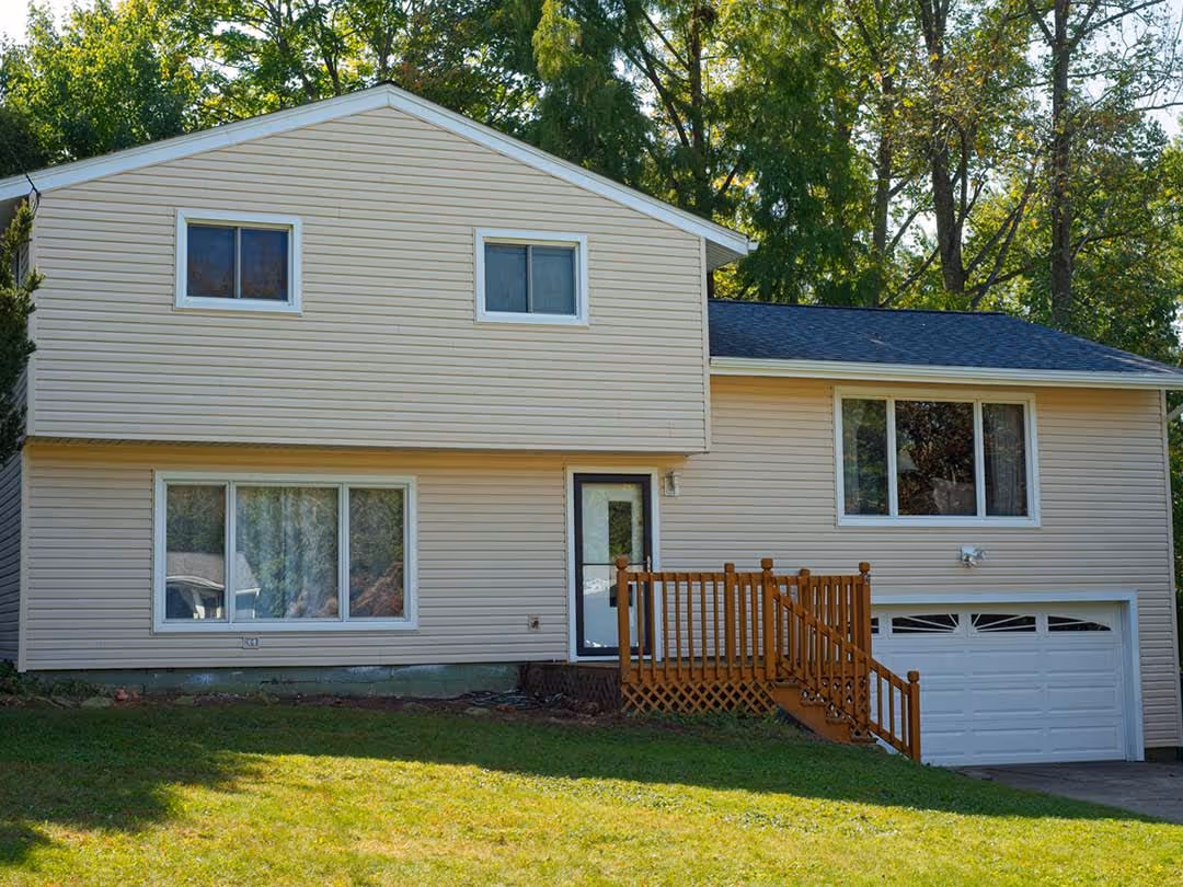 Two-story house with cream vinyl siding, white-framed windows, wooden porch railing, and attached garage.