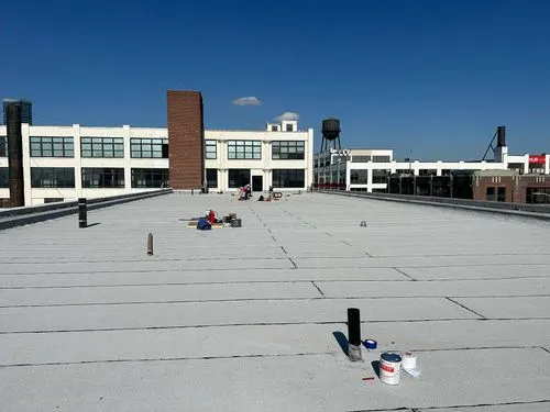 Workers installing a white flat roof on a commercial building under clear blue sky.