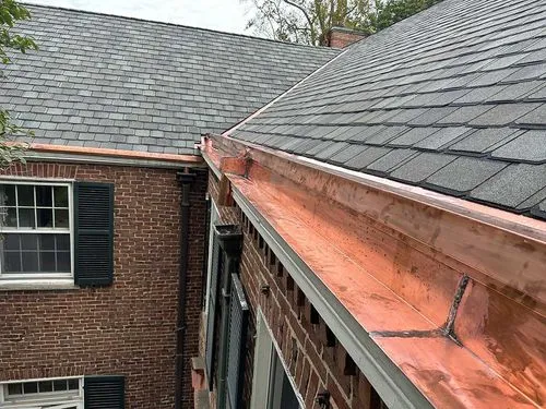 New copper gutter installed along the roofline of a brick house with gray shingles.