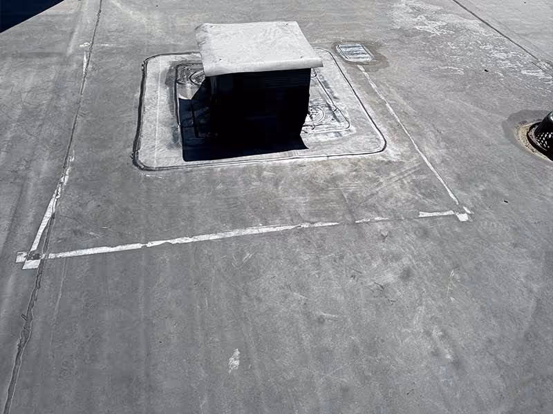 Flat gray roofing membrane with a vent pipe covered by a white cap and surrounding sealant.
