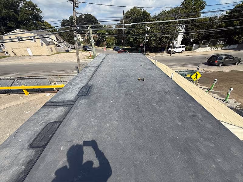 Flat rooftop with a grey surface, tools, and shadow of a person holding a smartphone.