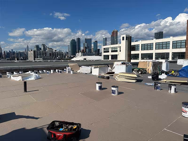 Construction materials and tools scattered on a flat rooftop with a city skyline in the background.