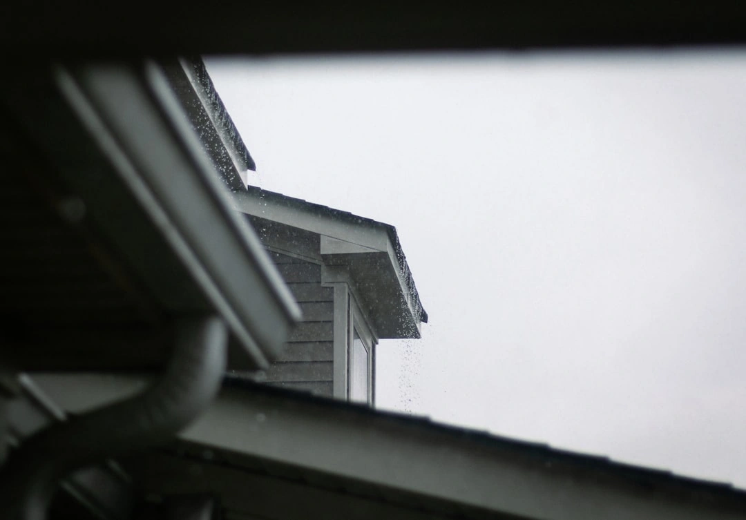 Professional gutter installation company workers carefully installing seamless gutters on a residential roofline Professional gutter installation company workers carefully installing seamless gutters on a residential roofline