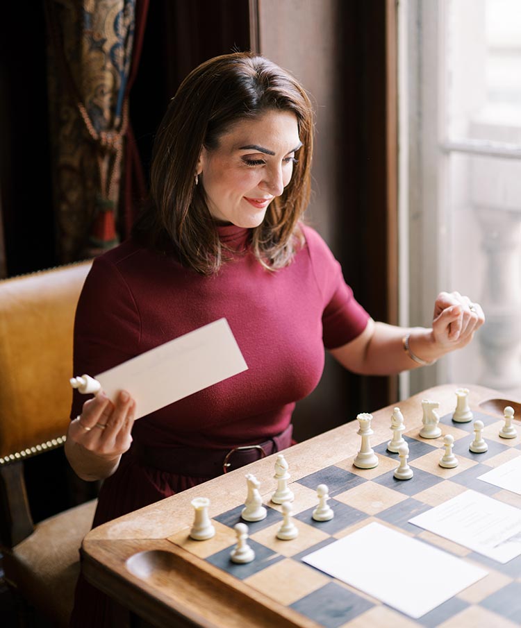 Philadelphia wedding planner Marian Braccia reviewing invitations beside a vintage chessboard next to a window