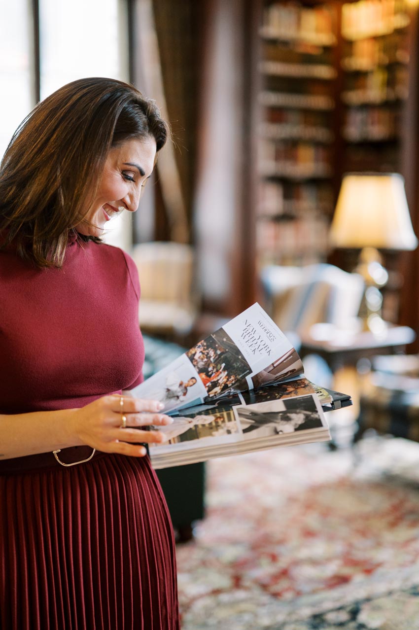 Luxury wedding planner Marian Braccia of Porch & Pearls browsing inspiration from a wedding magazine in a sophisticated library setting