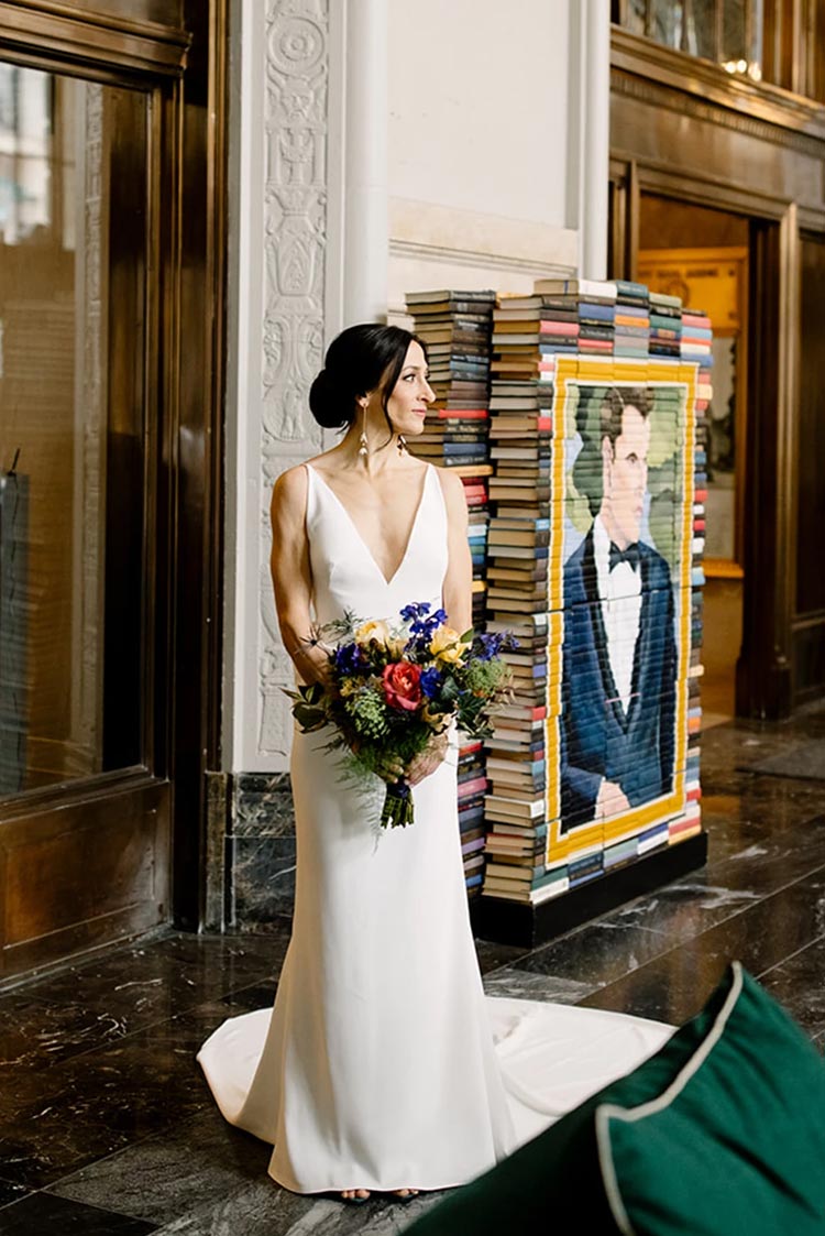 Elegant bride with colorful bouquet standing beside book art installation before her downtown Philadelphia wedding