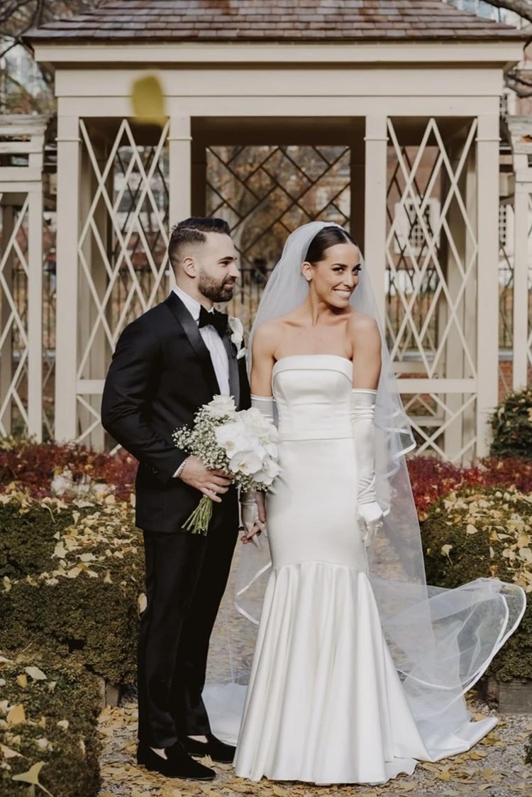Modern bride and groom standing in a garden gazebo with fall leaves and white florals