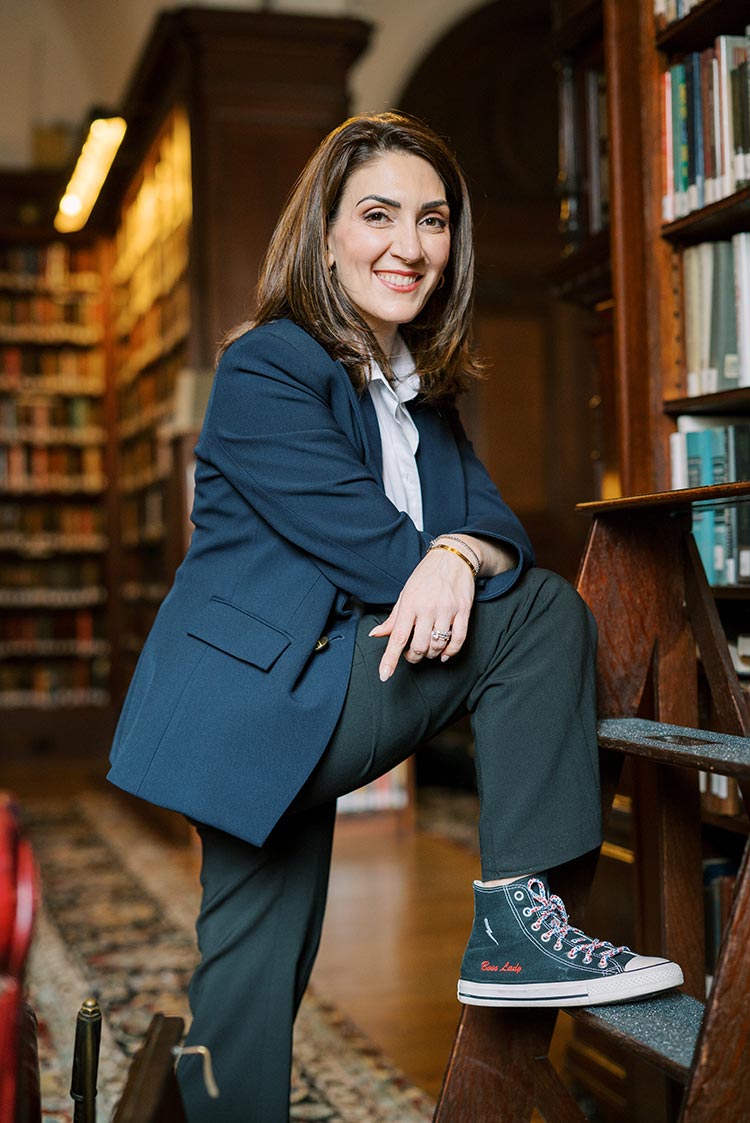 Marian Braccia in a navy blazer and sneakers that say 'boss lady' posing confidently in a historic library