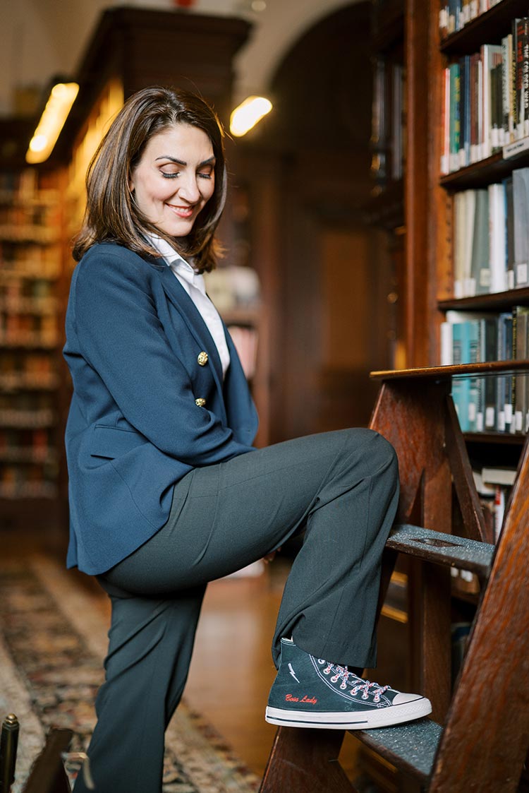 Marian Braccia in a navy blazer and sneakers that say 'boss lady' posing confidently in a historic library
