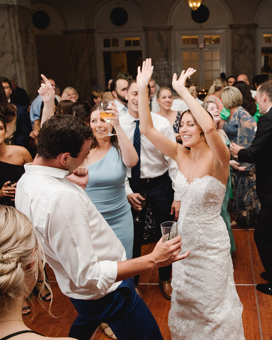 Bride and groom dancing with guests at a lively wedding reception, full of energy, laughter, and celebration.