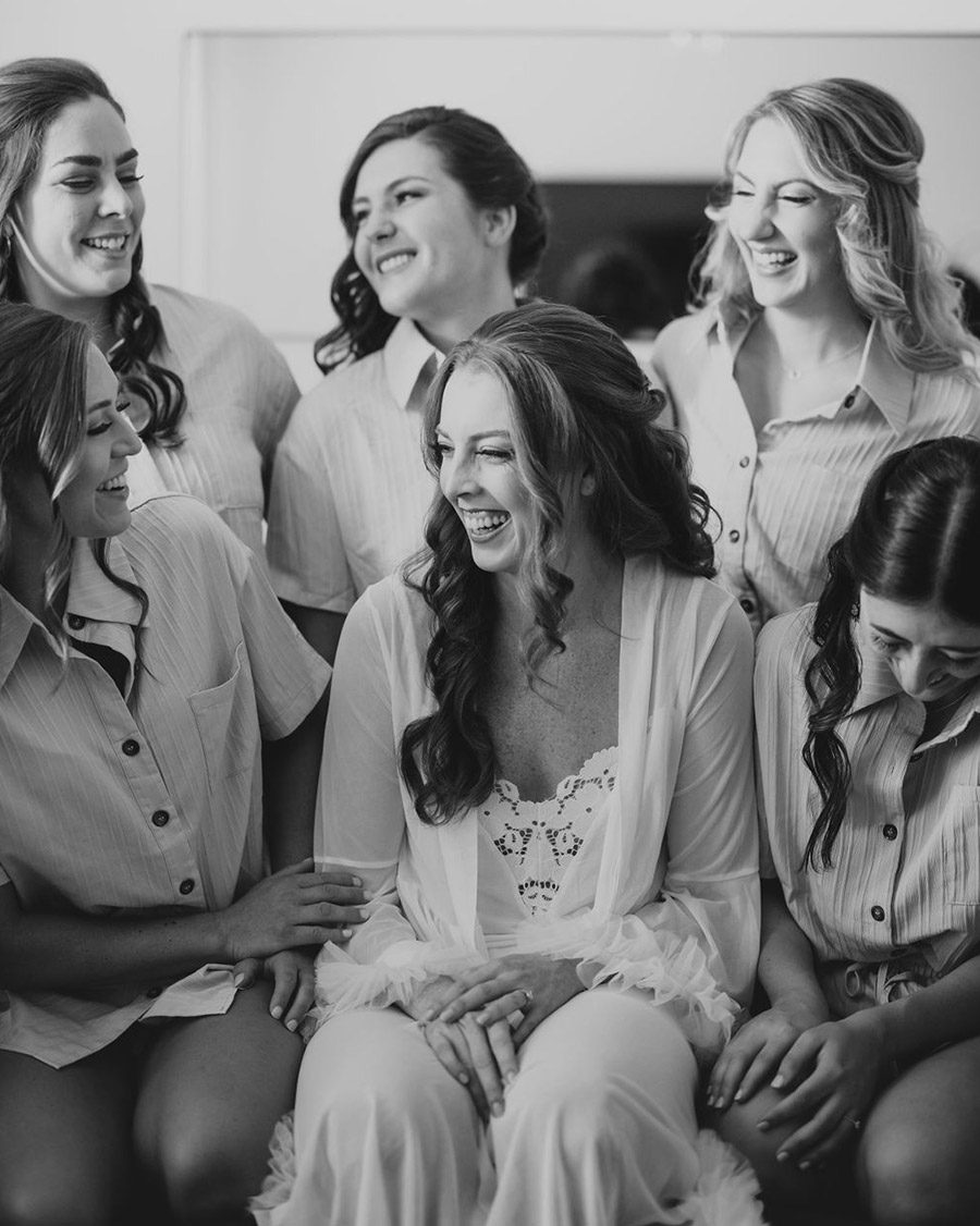Bride surrounded by her bridesmaids in matching outfits, sharing a joyful and intimate moment before the wedding ceremony.