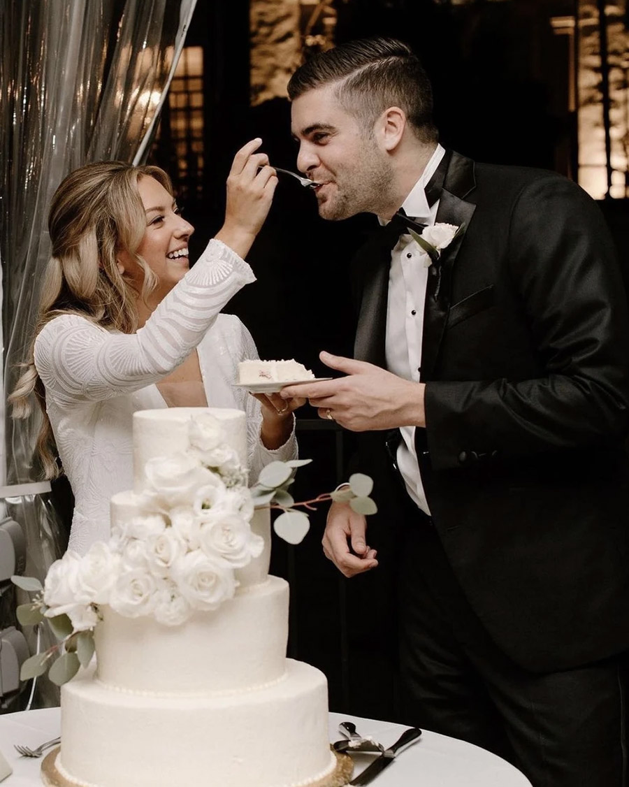 Bride and groom sharing a sweet moment during their cake cutting, with a beautiful cake decorated with roses in the foreground.