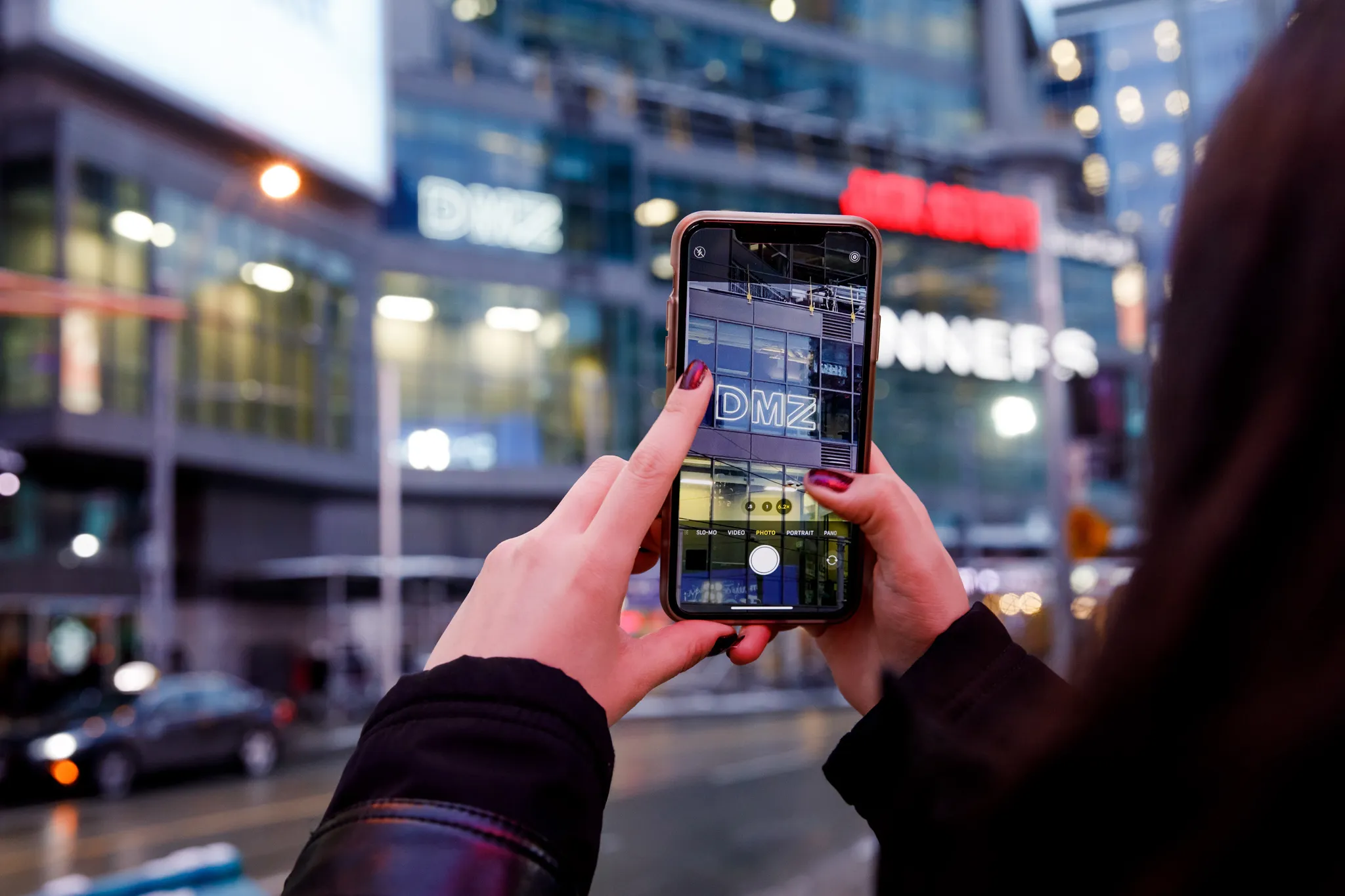 Person taking a photo of the DMZ building in downtown Toronto, highlighting DMZ’s roots at Toronto Metropolitan University and its global impact on entrepreneurship and innovation.