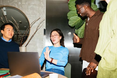 Three colleagues gathered around a laptop in a modern office, engaged in a friendly discussion.