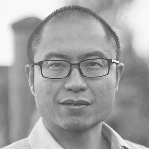 Close-up black and white portrait of a man wearing glasses and a collared shirt.