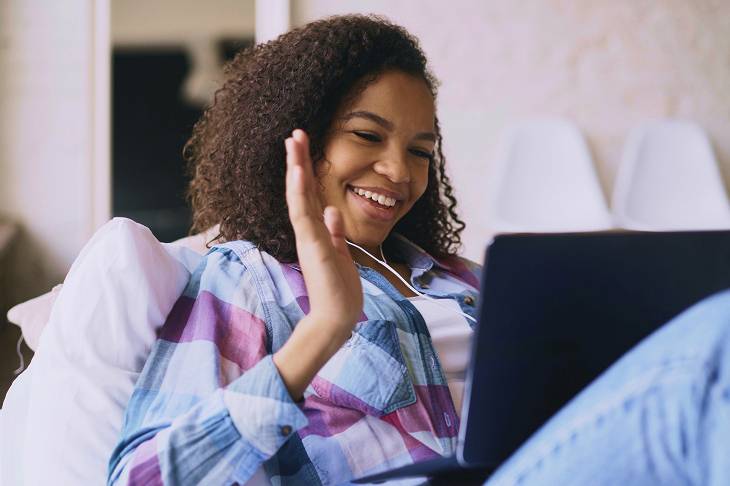 Smiling woman with curly hair waving during a video call on a laptop.