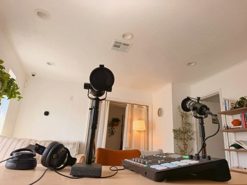 Podcasting setup with microphones, headphones, and sound mixer on a wooden table in a cozy room.