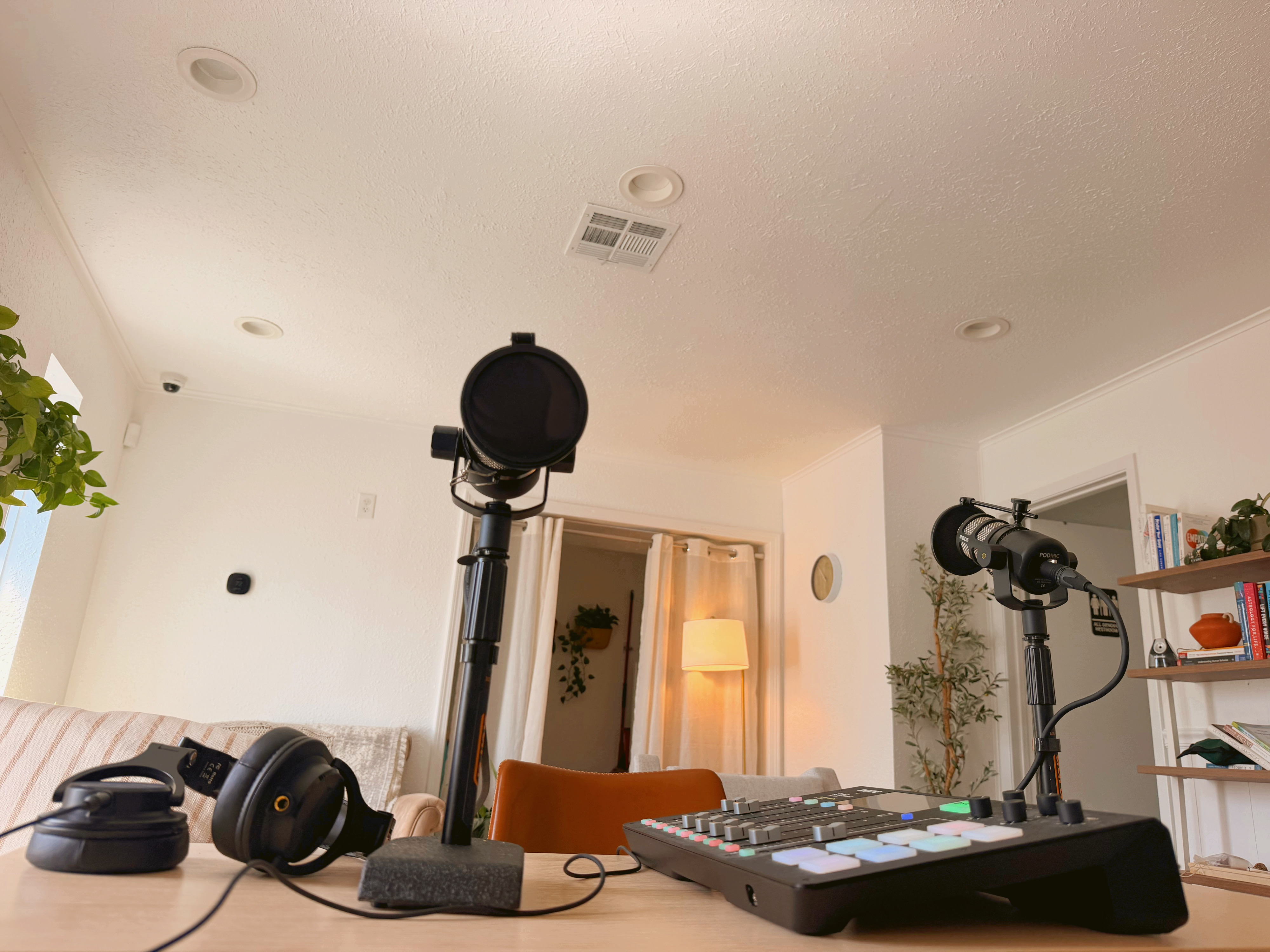 Podcasting setup with microphones, headphones, and sound mixer on a wooden table in a cozy room.