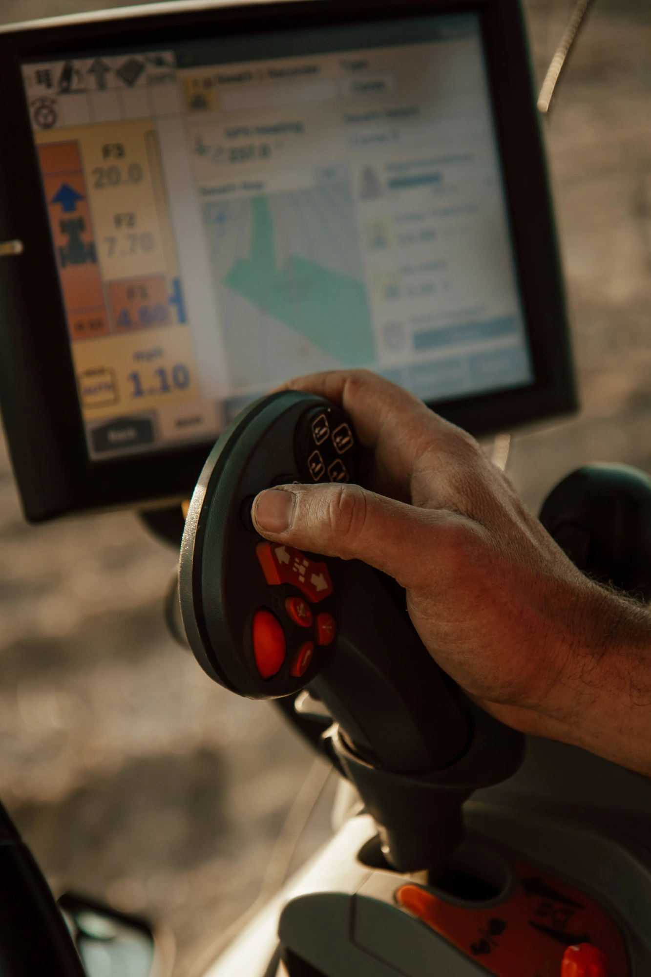 Hand on a tractor joystick in front of a precision ag guidance display