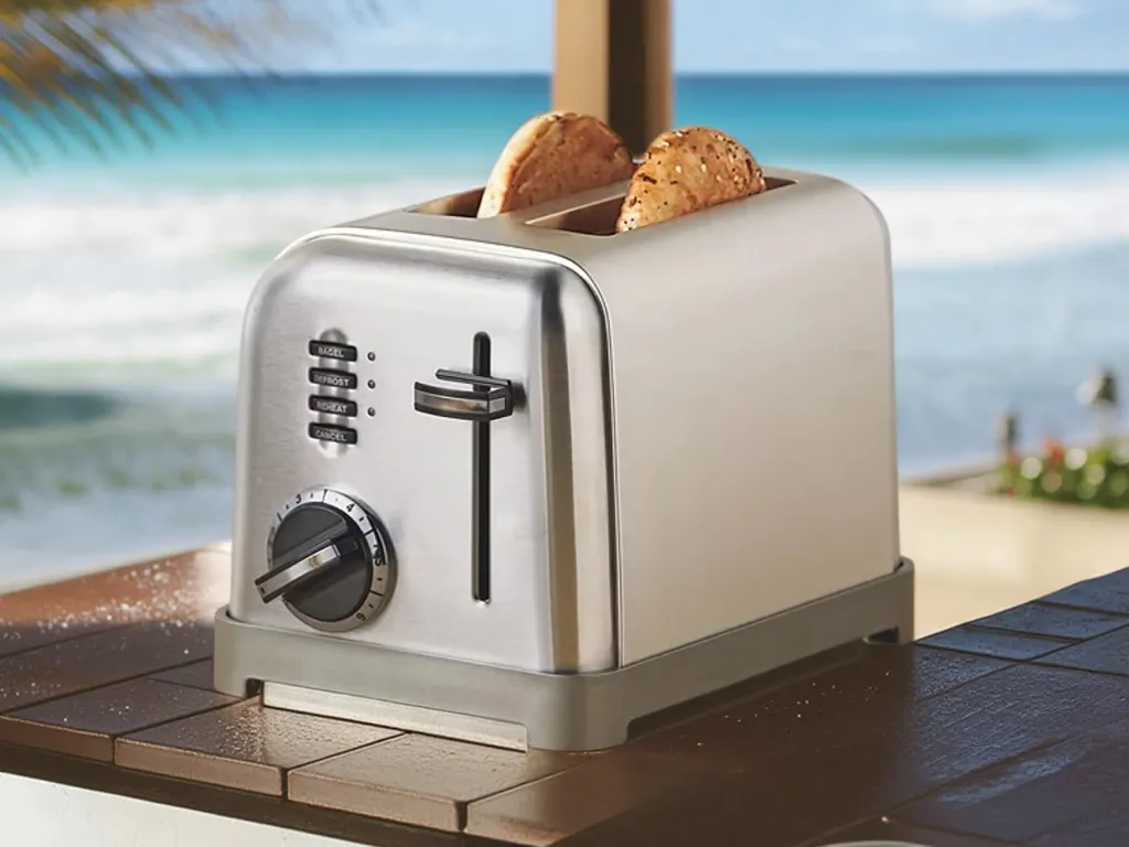 Silver toaster with two multigrain bread slices on a tiled surface with ocean waves in the background.