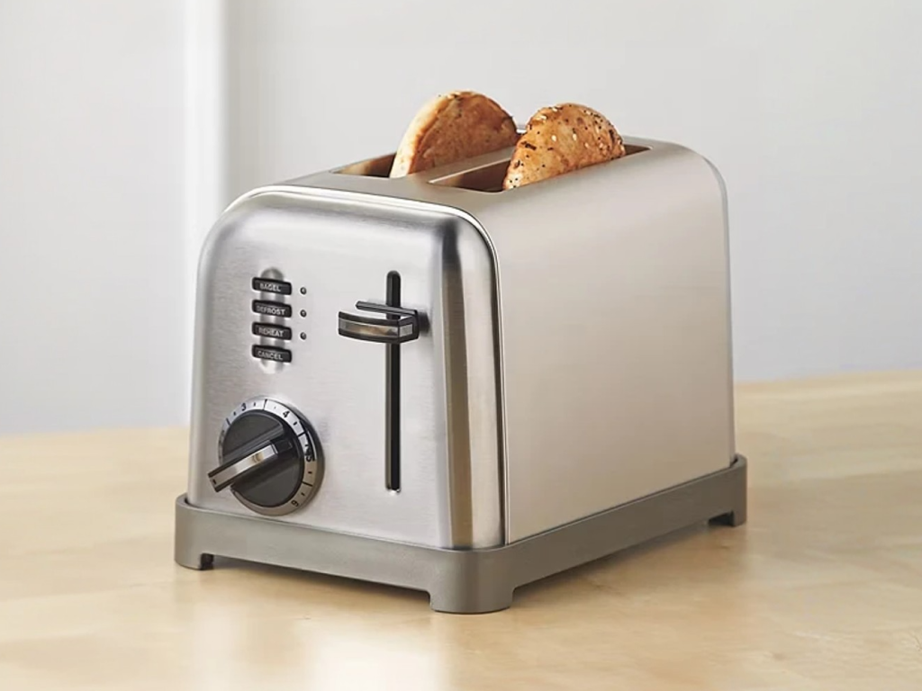 Silver two-slice toaster with control knob and buttons, toasting two pieces of seeded bread.