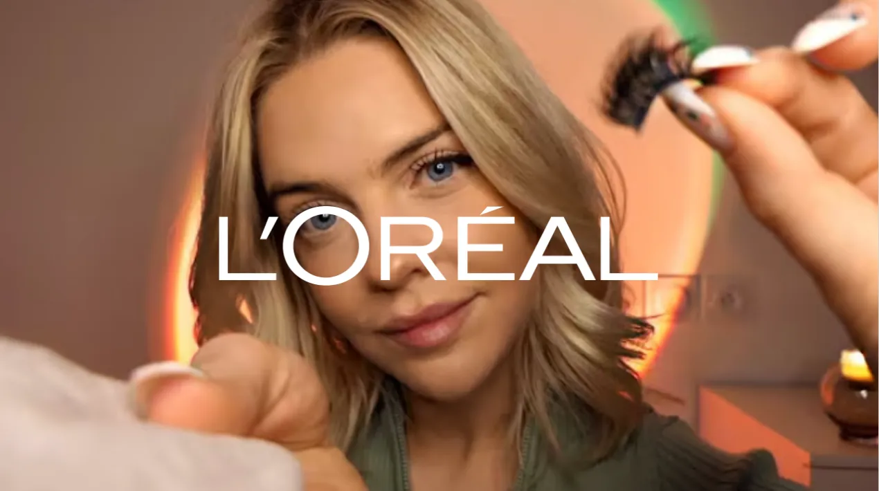 Jeune femme blonde aux yeux bleus tenant des cils postiches près de son visage avec le logo L'Oréal superposé.