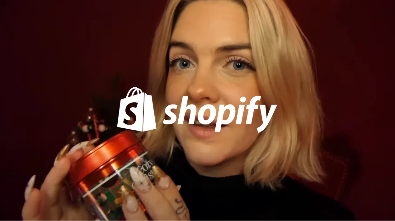 Une femme blonde tenant une boîte rouge avec des ongles décorés, fond sombre.