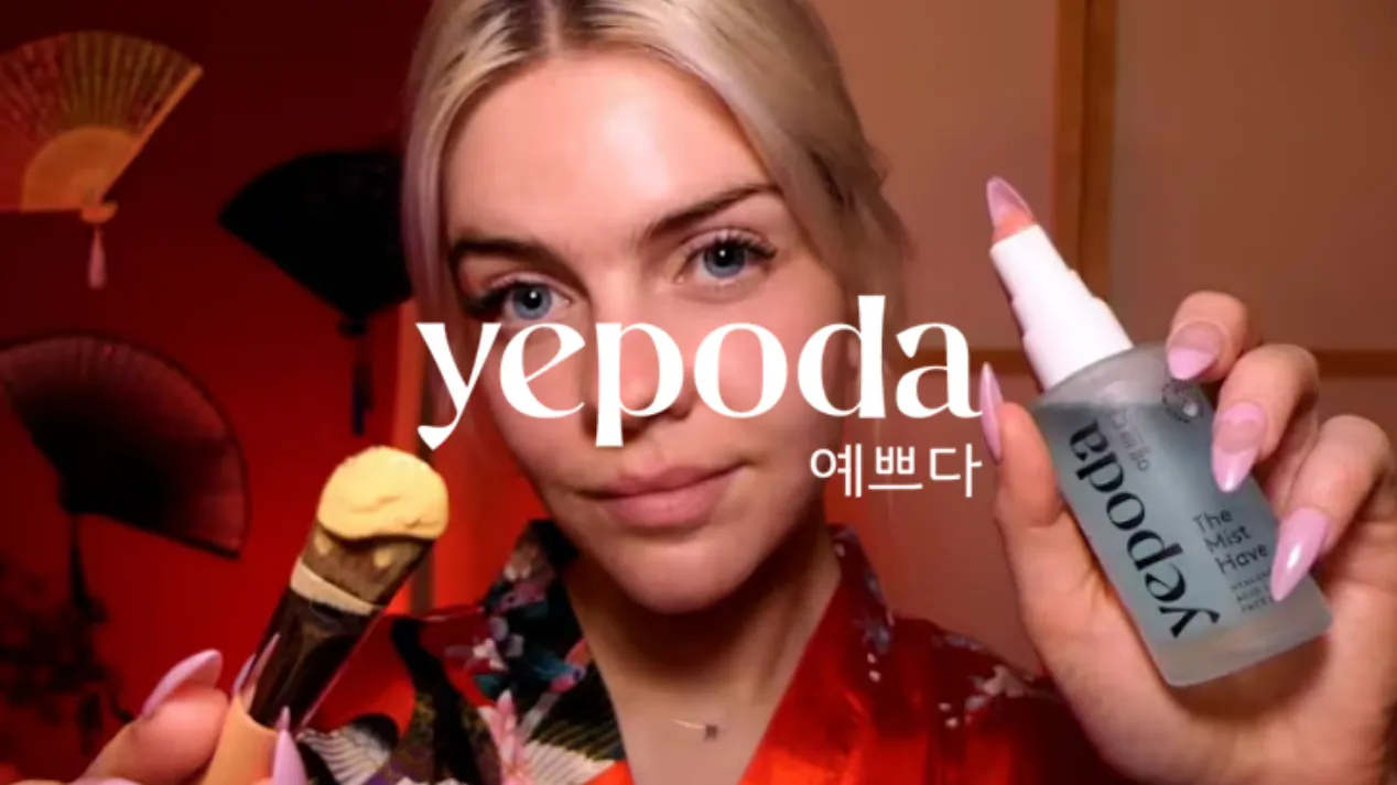 Jeune femme tenant un pinceau de maquillage avec du fond de teint et un flacon de spray Yepoda dans une pièce aux murs rouges.