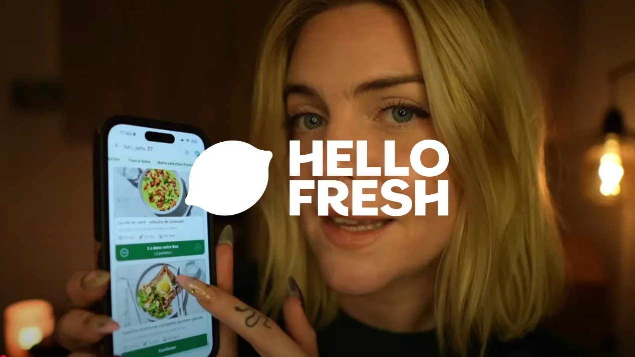 Femme présentant une application de recettes sur smartphone avec le logo Hello Fresh au centre.