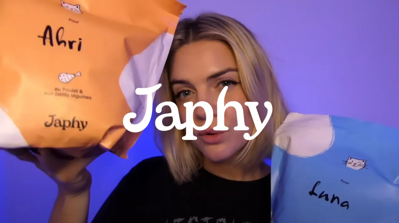 Une femme blonde tenant deux paquets colorés pour chats nommés Ahri et Luna sous une lumière violette, avec le texte 'Japhy' au centre.