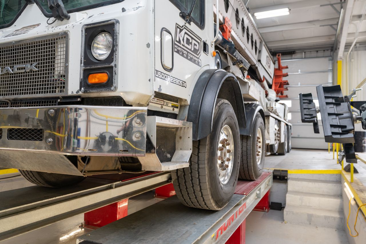 A concrete pump truck on a Hunter alignment rack inside a brightly lit repair shop, ready for inspection or alignment service. 