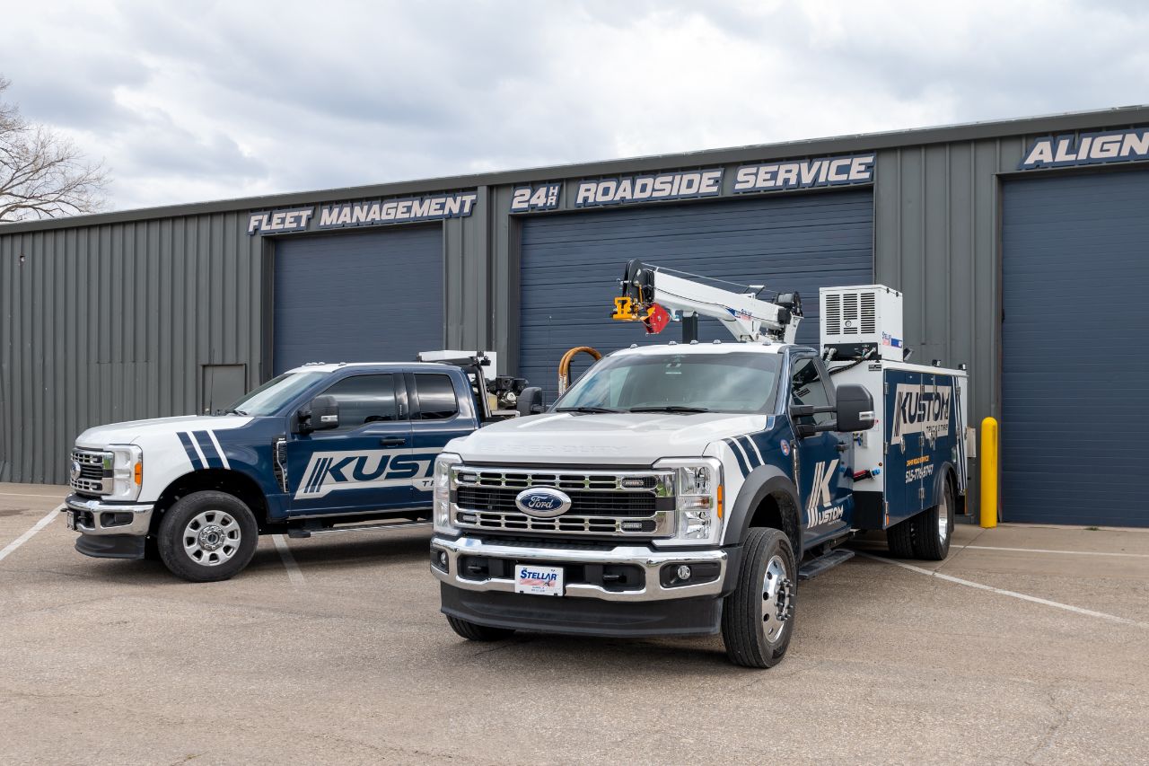 Two Kustom Truck and Tire service vehicles parked outside shop with signage for fleet management, 24-hour roadside service, and alignment services.